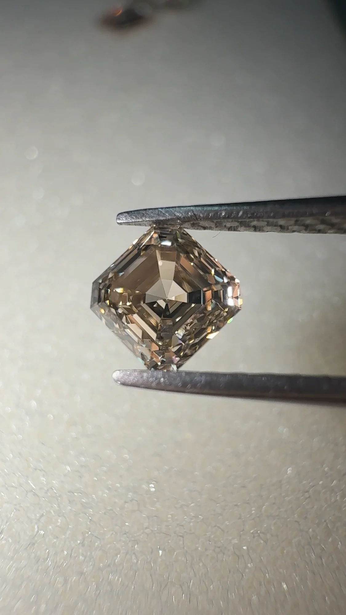 Champagne asscher cut diamond held face-up in tweezers