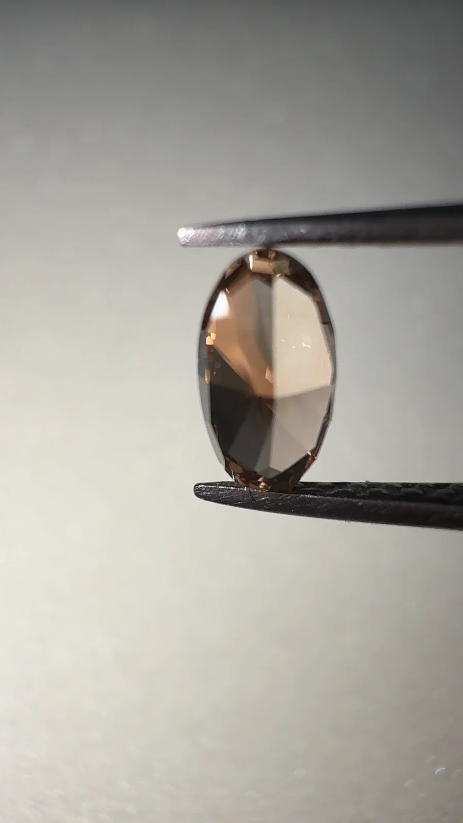 A champagne oval diamond held in tweezers on our desk