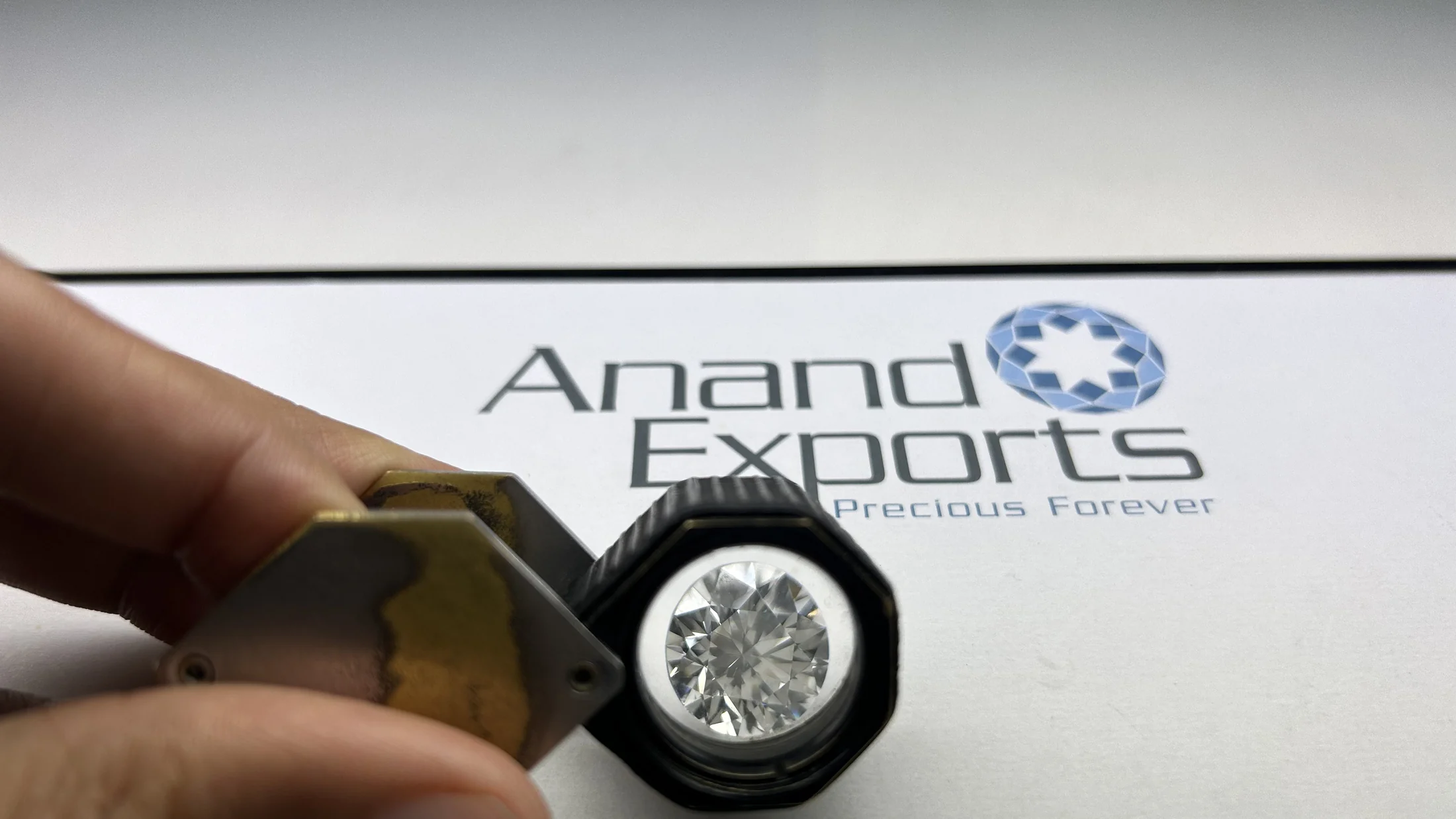 A diamond under a loupe in front of the Anand Exports card