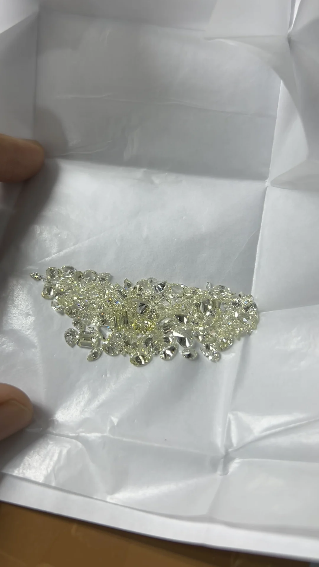 A hand opening a white diamond parcel paper full of polished stones