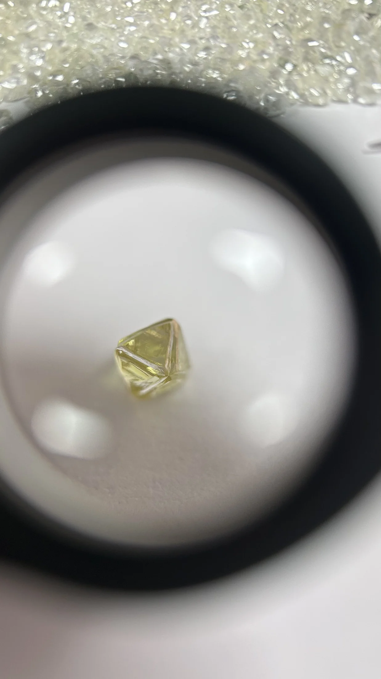 A yellow rough diamond octahedron inspected under a 10x loupe